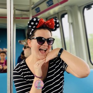 Fun woman wearing Minnie Mouse ears and sunglasses on a Disney transportation ride, enjoying a vacation.