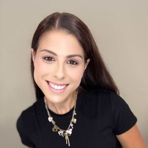 Beautiful smiling woman with brown hair wearing a black top and stylish jewelry.